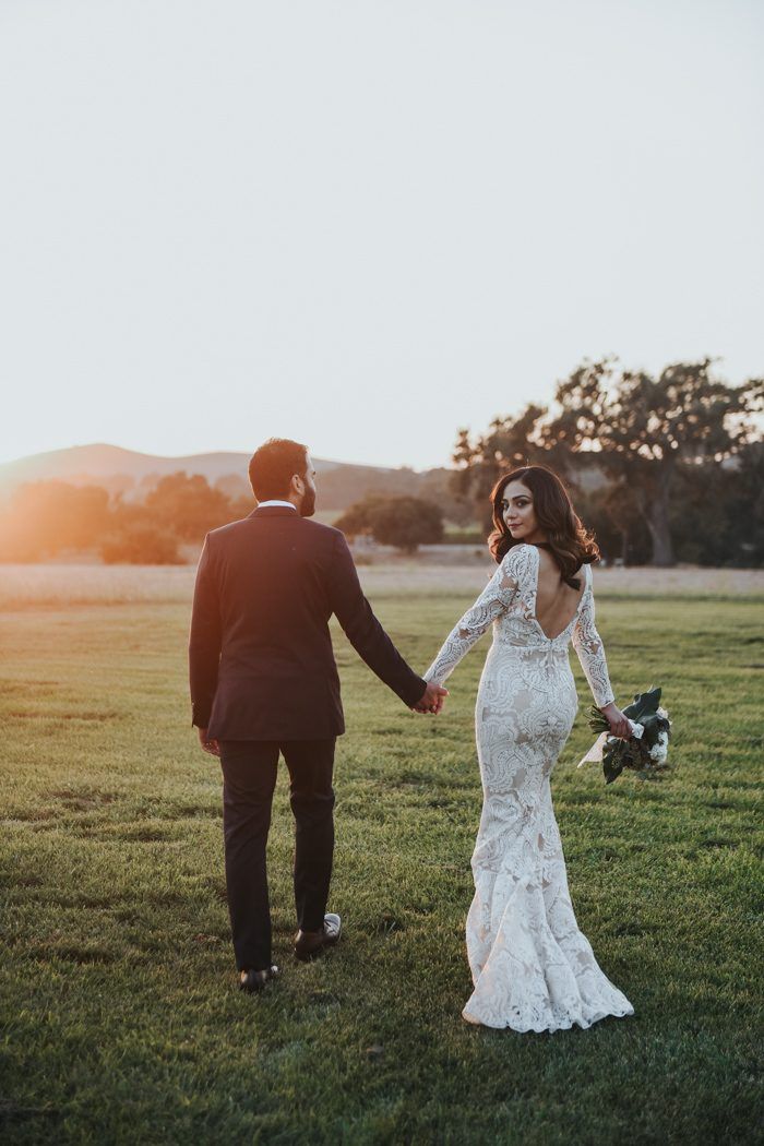 Backless lace gown and slim dark suit walking into golden light