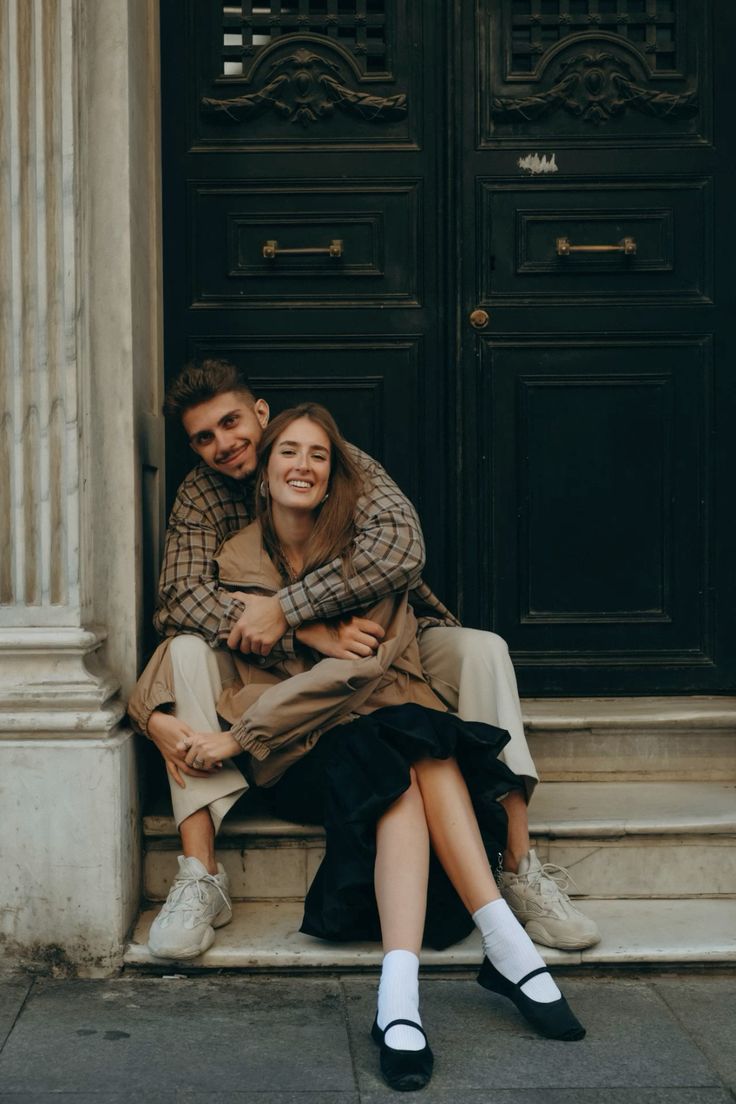 Couple on stone steps by a carved dark door, checked shirt and brown jacket