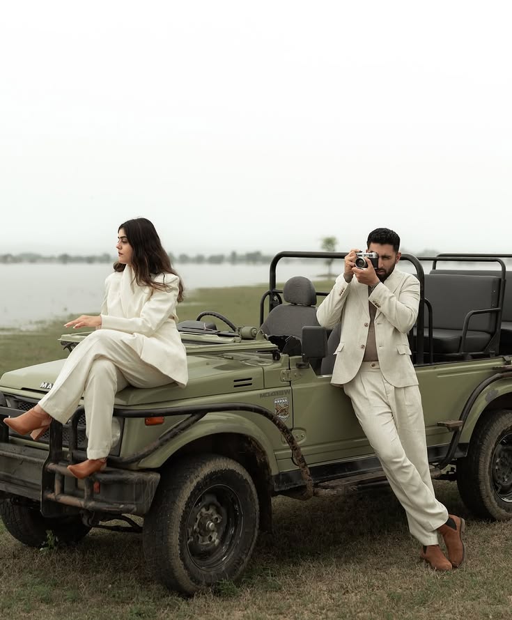 Ivory suits leaning against an olive safari jeep by still water