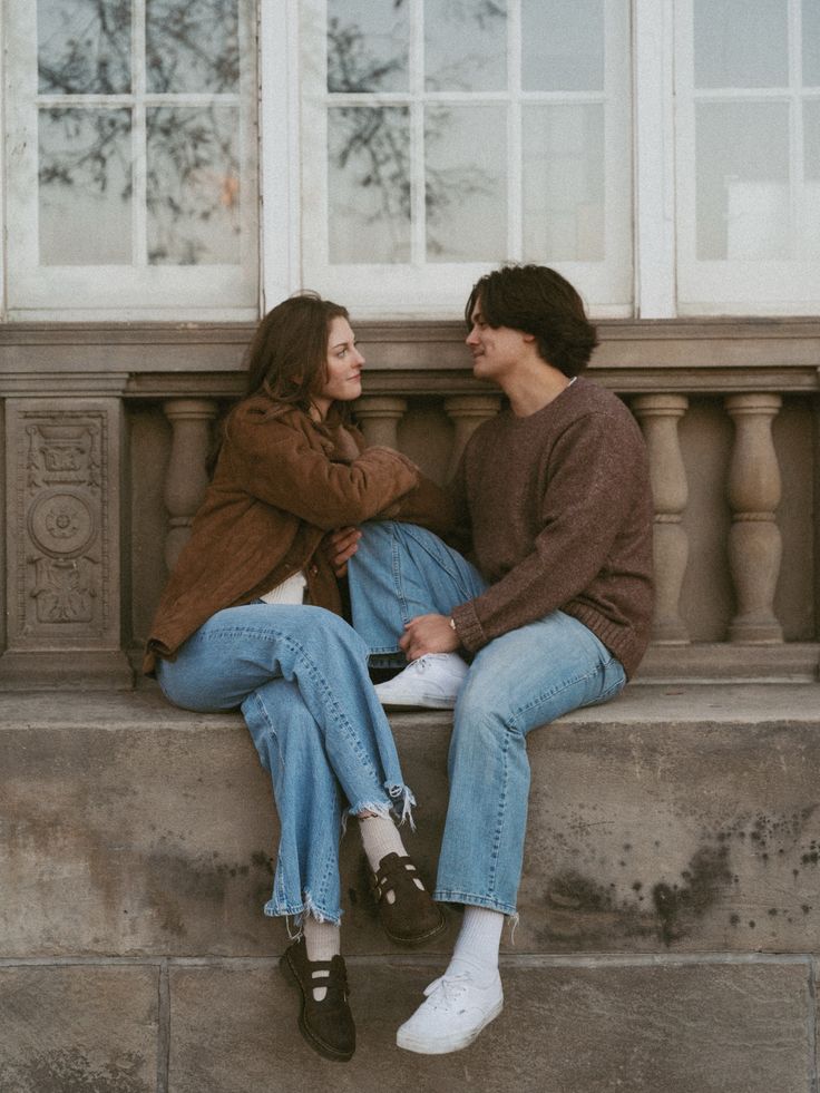 Couple sitting on a stone balustrade in brown layers and blue jeans